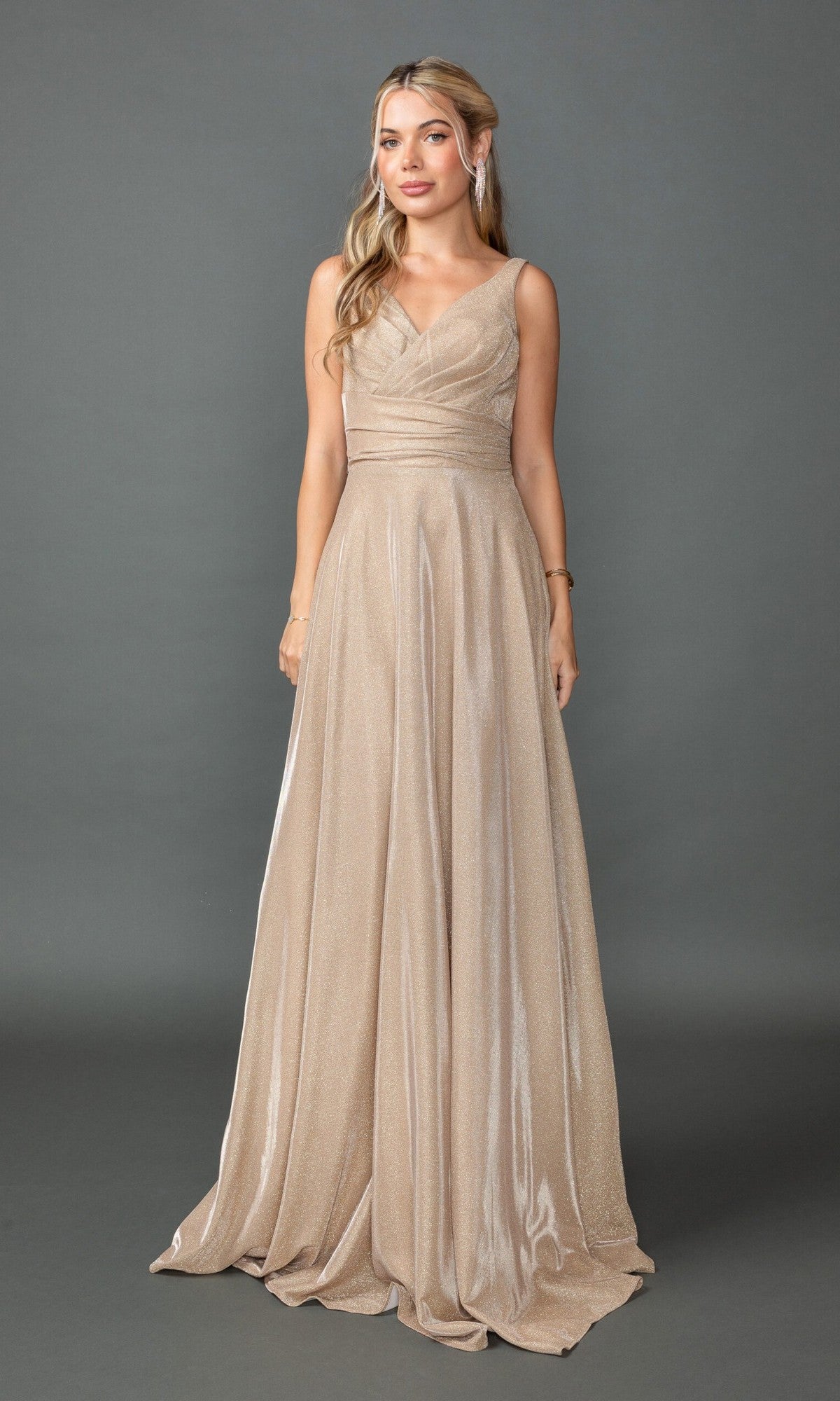 Woman wearing the Long Prom Dress: Dancing Queen 4545, a champagne floor-length gown with a V-neckline, gathered waist, and sleeveless design, standing against a gray background.